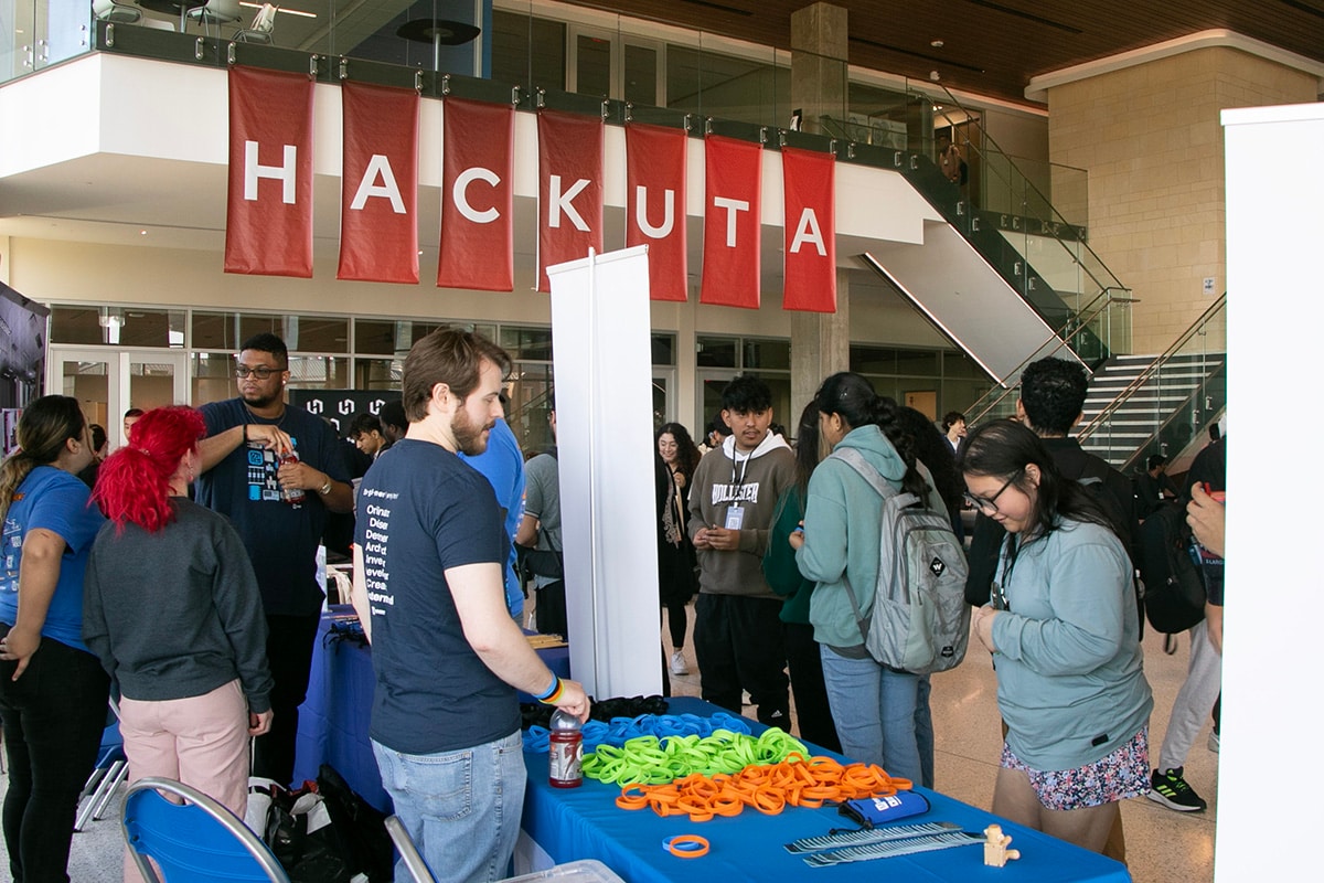 Students standing at booths at Hack UTA event - opens in a new tab